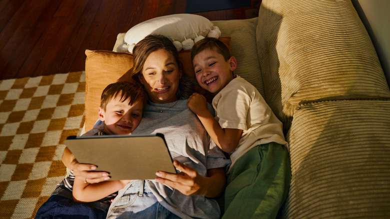 A family lying on a couch watching a movie on a tablet together