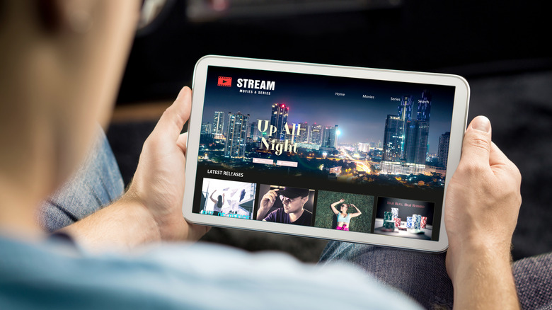 A man holding a tablet showing a streaming movie service on the screen