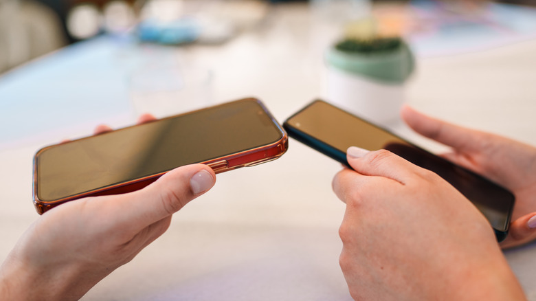 Two hands holding cell phones with different color cases.