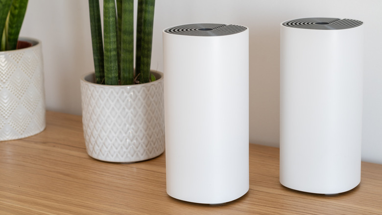 Two mesh Wi-Fi system nodes on a wooden desk next to potted plants
