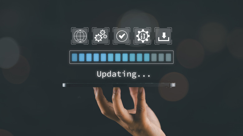 A hand propping up a thin device with a progress bar and a message indicating an ongoing update projected above.