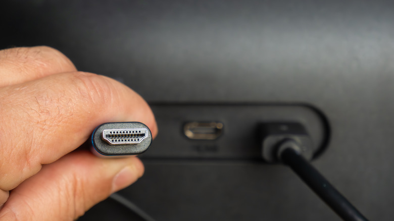 A person holding one end of an HDMI cable. They're standing behind a TV or monitor.