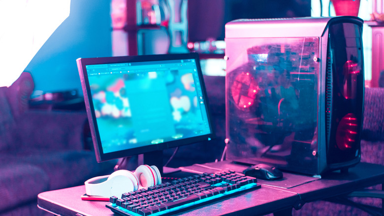 Gaming PC setup with RGB lighting, desktop tower, monitor, keyboard, mouse, and headphones on a desk.