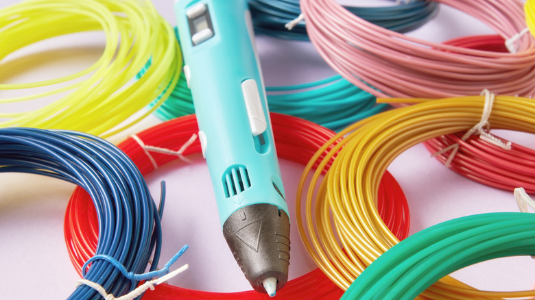 Close up of a 3D printing pen next to plastic filament reels.