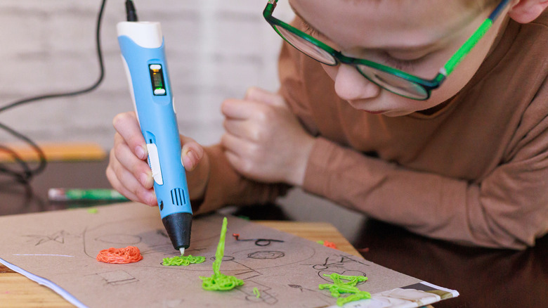 A child focused on creating small objects with a 3D printing pen.