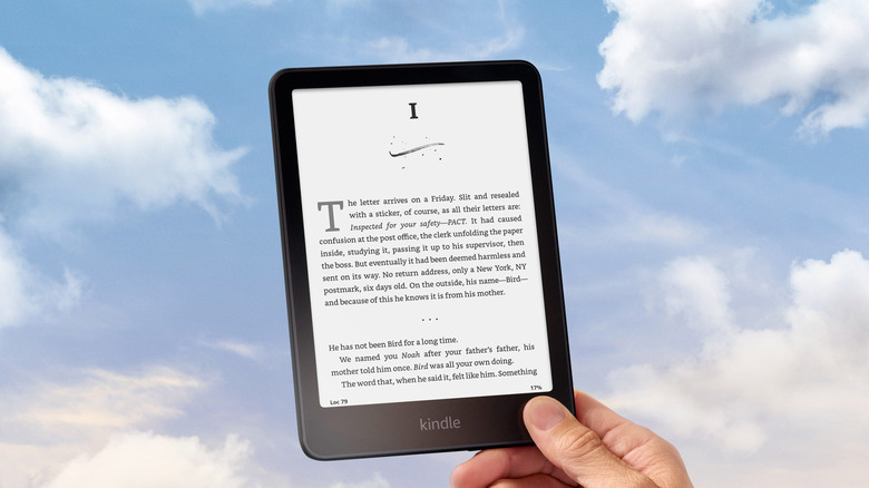 A hand holding the Kindle Paperwhite over a blue sky background