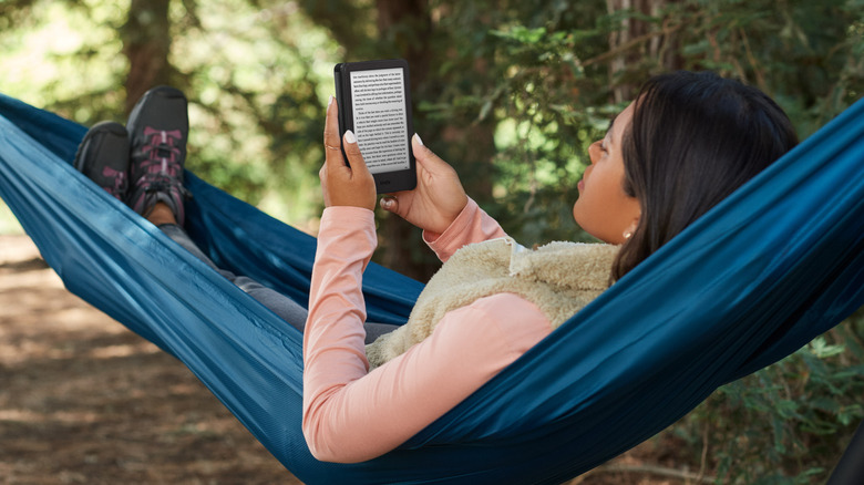 A woman sitting in a Hammock reading a Kindle in the woods