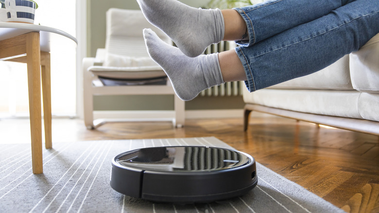 A person lifting their feet to let a robot vacuum through.