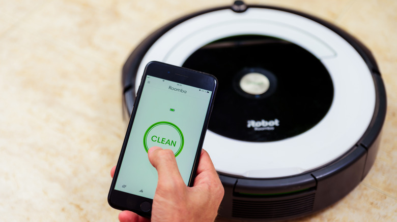 A person uses a smartphone app to operate a robot vacuum.