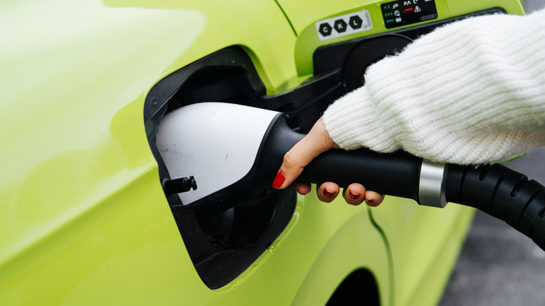 a woman's hand is charging her bright green EV