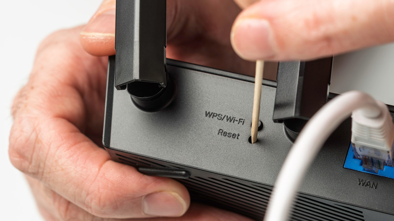 Someone inserting a toothpick in the pinhole at the back of the router to reset it.
