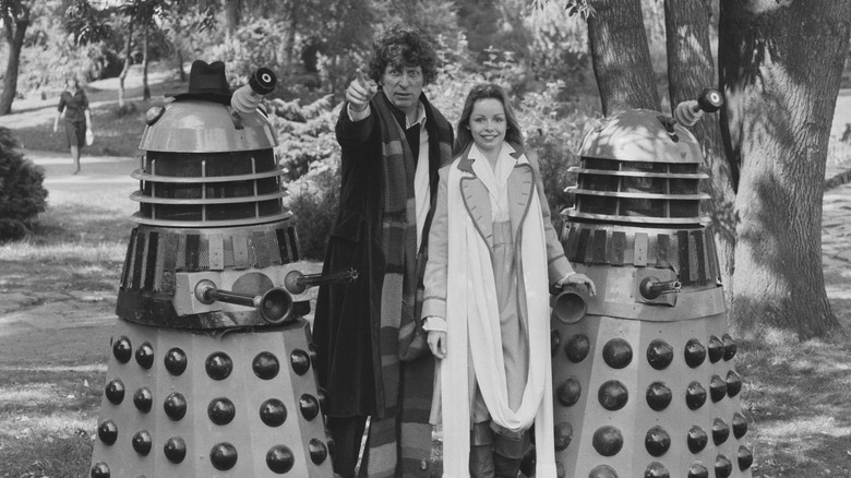 Tom Baker and Lalla Ward stand between two Daleks