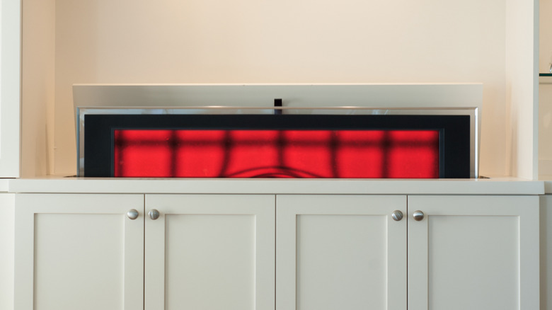 A TV emerging from an off-white cabinet in front of a cream-colored wall.