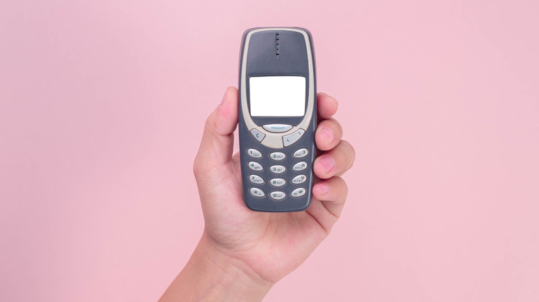 Hand holding old Nokia phone model against pink background