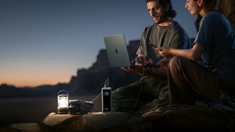 Two people using a Prime Power Bank to power a laptop at a camping site