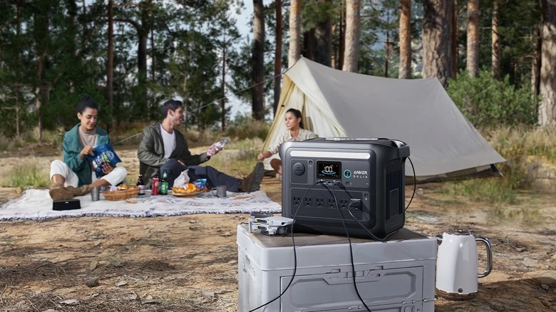 An Anker SOLIX C1000X Portable Power Station connected to camping devices with people camping in the background