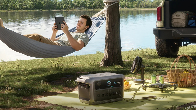 A man in a hammock next to an Anker SOLIX C2000 Gen 2 Portable Power Station at an outdoor campsite