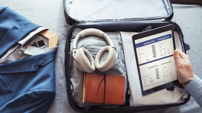 a hand holding an iPad over an open suitcase