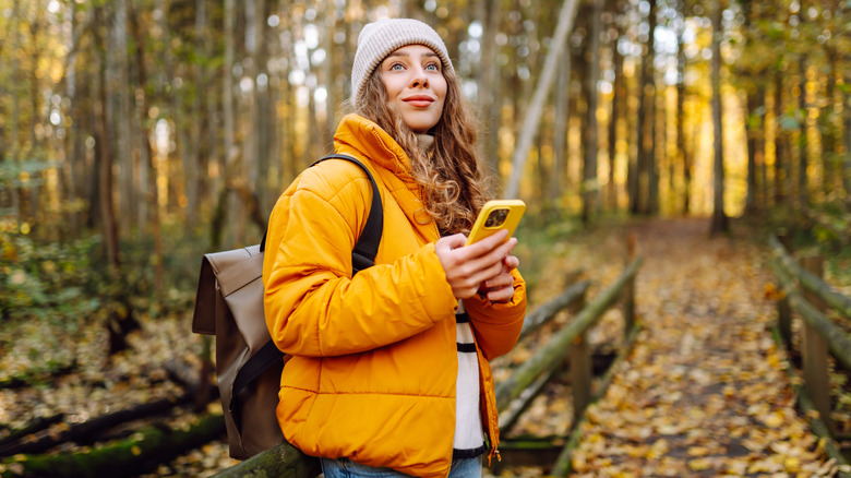 A woman on a forest hiking trail with a yellow coat holding her phone