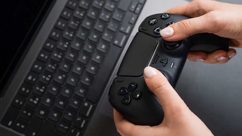 Woman holding black DualSense 5 controller with MacBook Pro in background