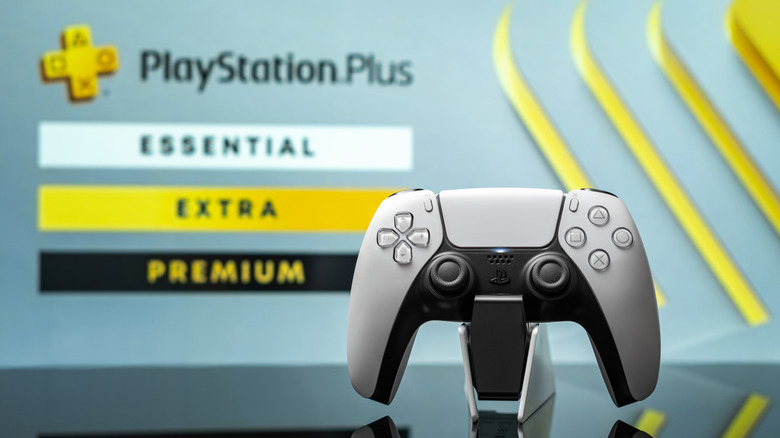 A picture of a DualSense controller on a charging dock, with the PS Plus hero image in the background showing all the tiers