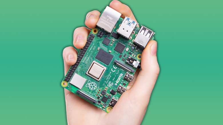 A Raspberry Pi 4 microcontroller being held in a person's hand on a solid light green background.