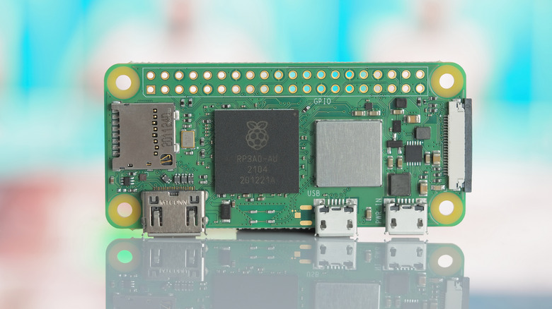 A Raspberry Pi Zero 2 W stood up on a reflective surface against a blurry blue-white background.