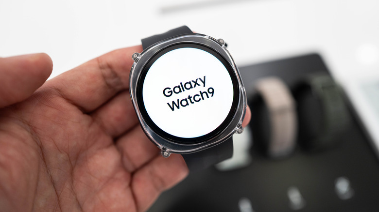 Galaxy Watch 9 held in hand showing screen with logo on white background