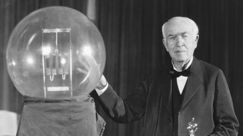 Thomas Edison posing with incandescent bulb replica