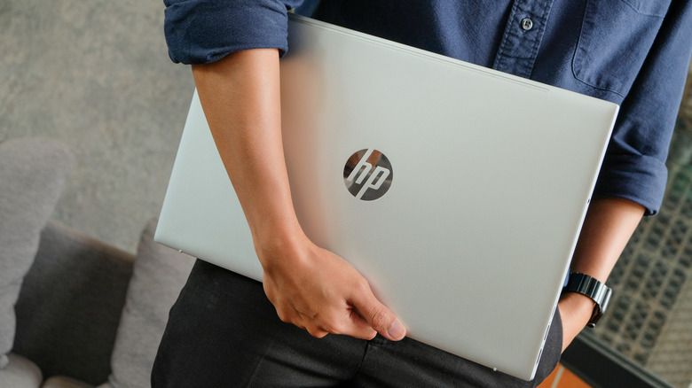 A man with folded sleeves carrying a laptop from HP