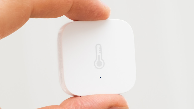 Person holding an Aqara temperature smart sensor.