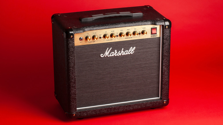 A black-and-gold Marshall amplifier, upright, against a red backdrop.