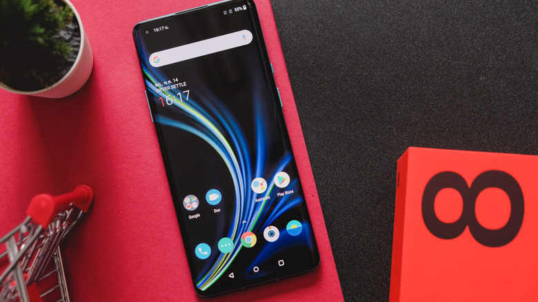 A OnePlus phone with the screen turned on lying beside the package it comes in