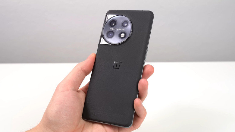 A person holding a black OnePlus phone against a grey and white background