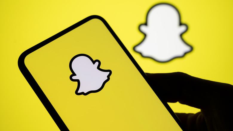A mobile phone showing the Snapchat logo on the app's loading screen.