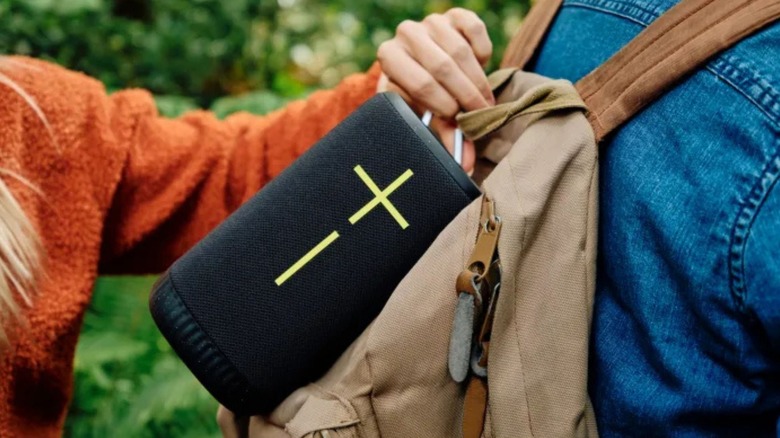 A person attaching an Ultimate Ears speaker to a hiking bag