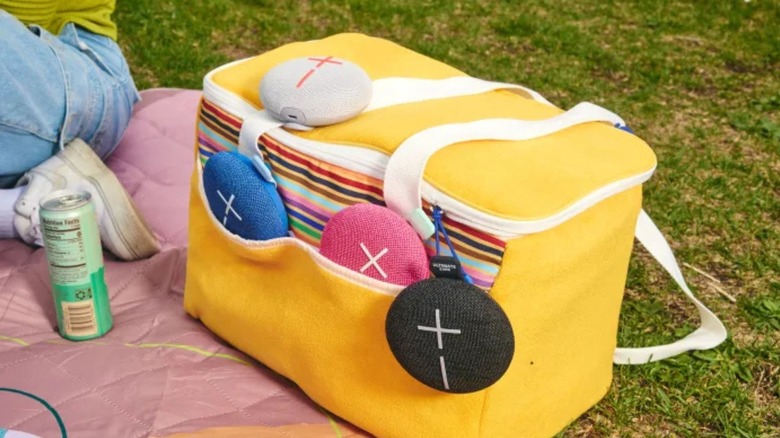 Several Logitech/Ultimate Ears speakers attached to a yellow cloth cooler on a picnic blanket