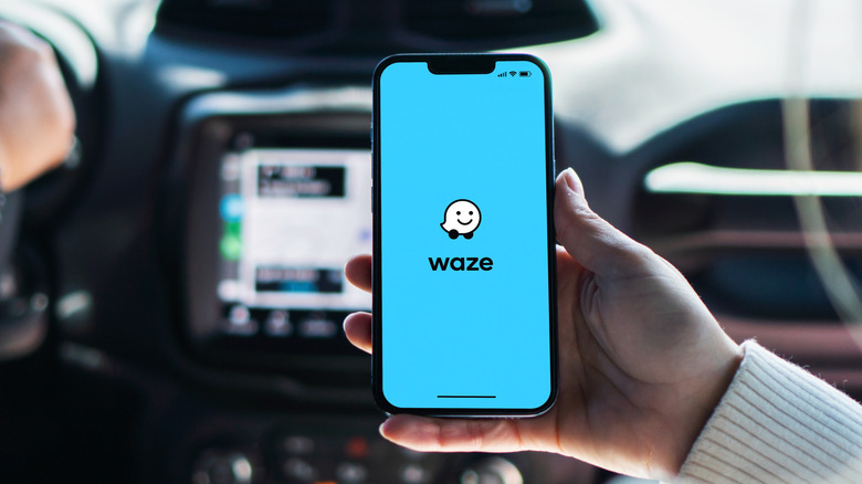 A person in a car holding a smartphone with Waze on its display.