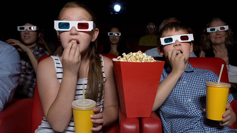 Picture of a cinema showing two kids with 3D glasses on eating popcorn while watching a movie