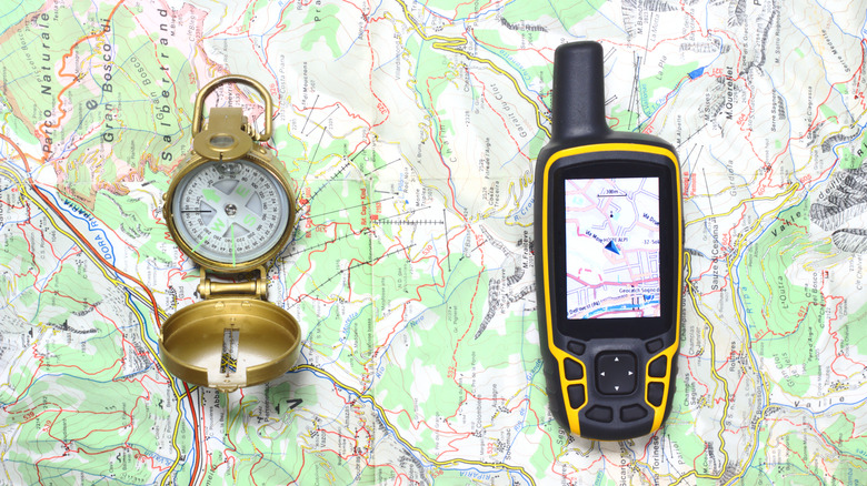 Handheld GPS device placed on a map with an analog compass nearby.