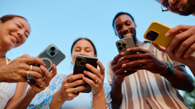 An low-angle view of four people looking at their phones and smiling.