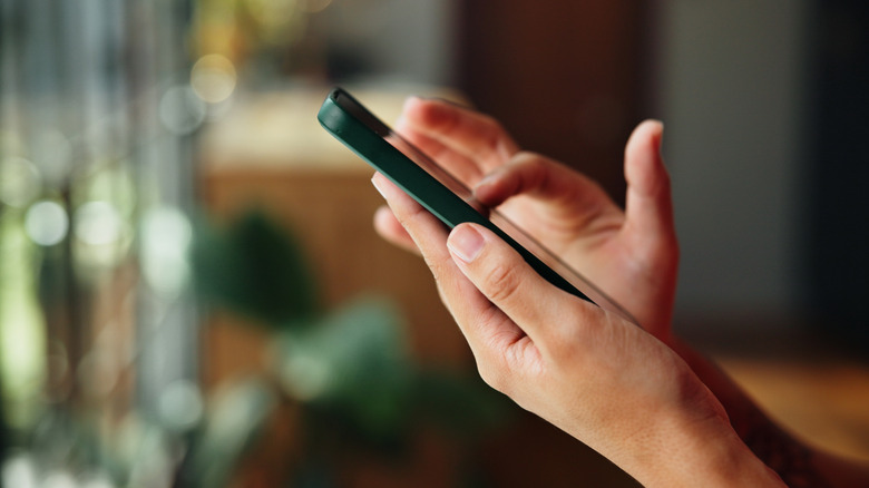 A side view of hands holding a phone, a finger on the screen.
