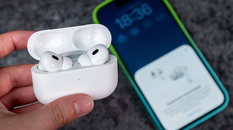 A person holding an AirPods Pro charging case with both earbuds inside. An iPhone is on the counter behind the AirPods.