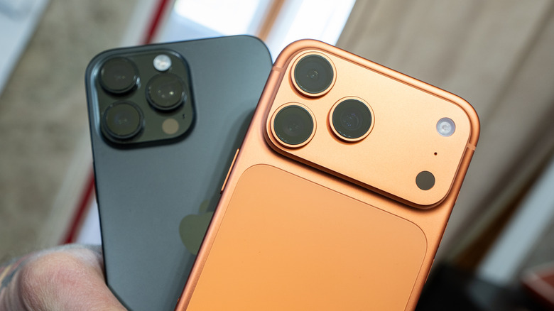 A hand holding an iPhone 16 Pro Max and an iPhone 17 Pro Max.