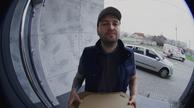 Video doorbell live feed of pizza delivery person waiting.