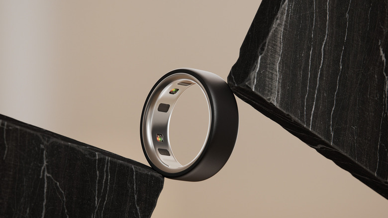 A black Oura ring is pressed between two black slate slabs.