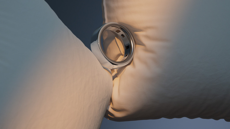 A silver Oura ring sits snugly between two pillows.