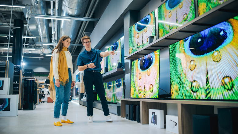 Two people looking at TVs stacked on shelves in an electronics store