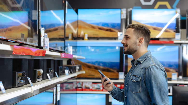 A person holding a smartphone and looking at TVs in an electronics store