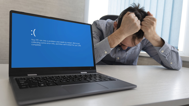 A person gripping their hair in frustration due to a laptop not working properly and showing a blue screen with an error message